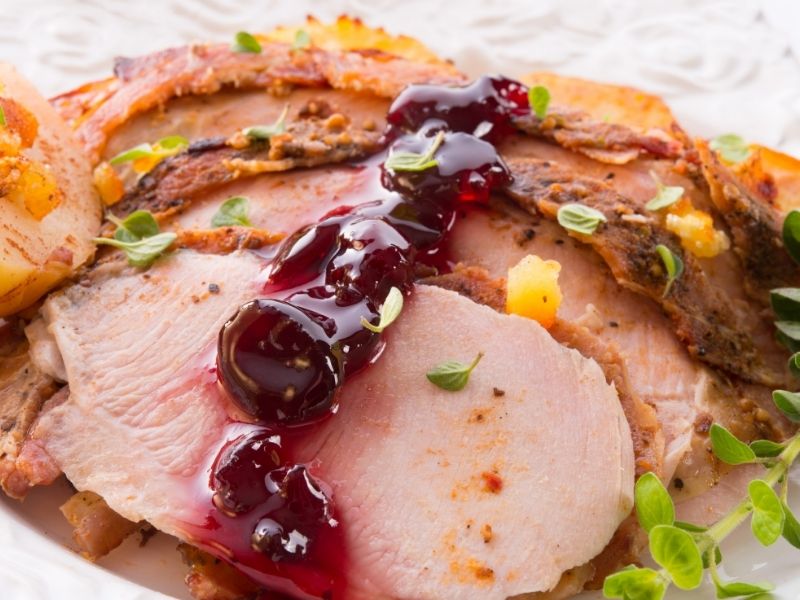 cut roasted turkey on a plate with cranberry sauce.