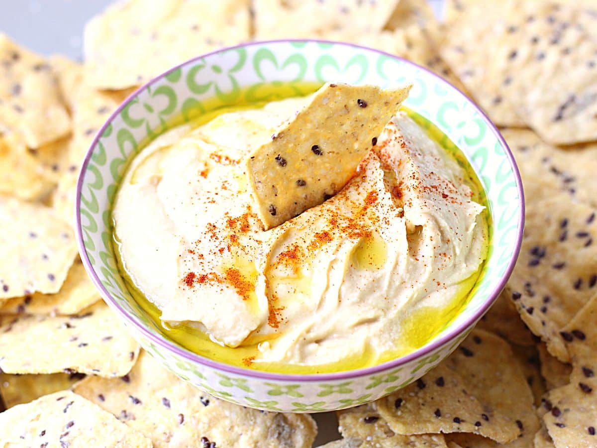 Blender hummus in a bowl with a pita chip.