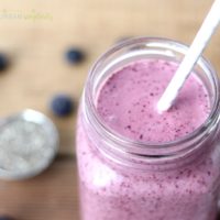 Metabolism Boosting Blueberry Smoothie in a mason jar with a straw. Chia seeds are scattered in the background.