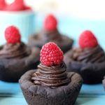 Four dark chocolate cookie cups topped with a red raspberry.