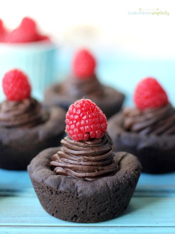 Four dark chocolate cookie cups topped with a red raspberry.