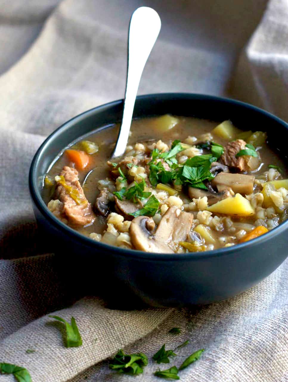 Slow Cooker Beef and Barley Soup in a bowl with a spoon sticking out. 