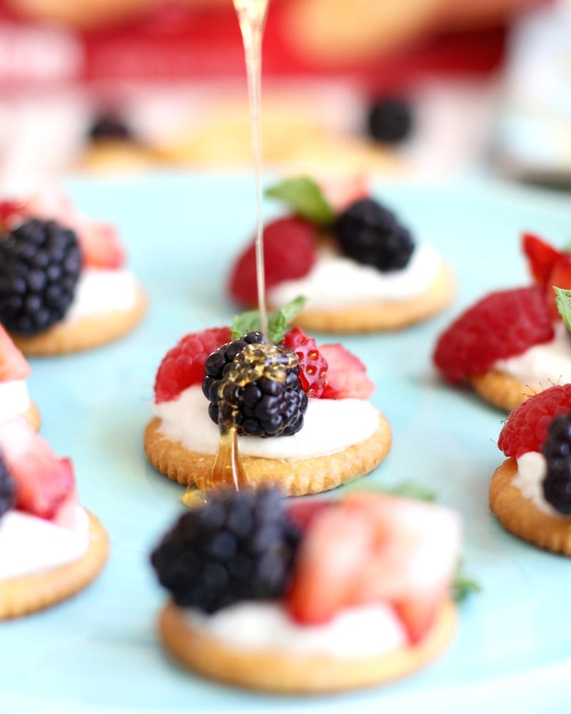 Ritz Crackers being with berries and cream being drizzled with honey