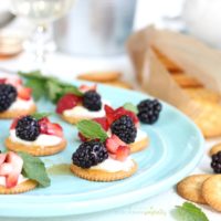 Plate full of crackers topped with berries and cream.