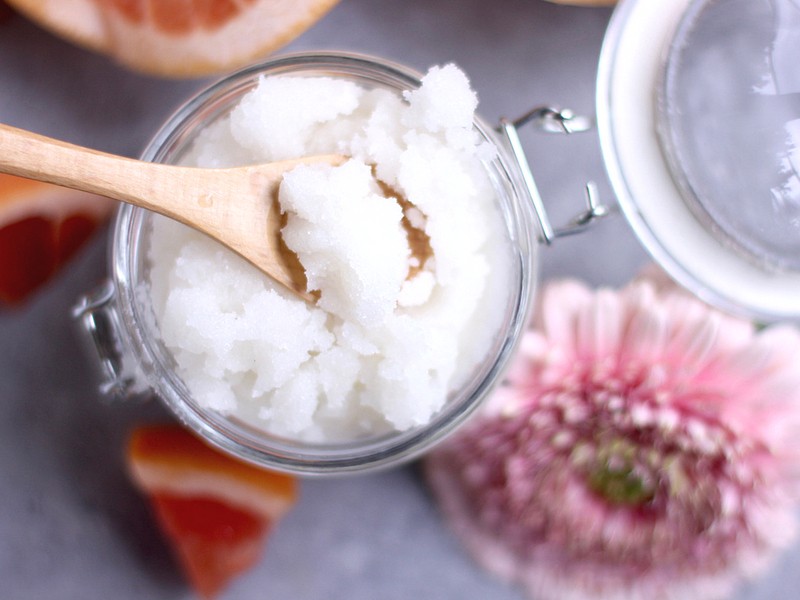 Top view of a jar of grapefruit sugar scrub with a flower next to it.