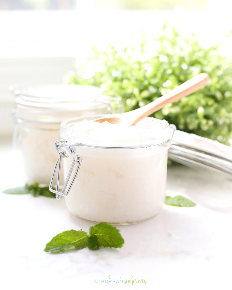 Two jars of mint sugar scrub on a counter with mint leaves in front.