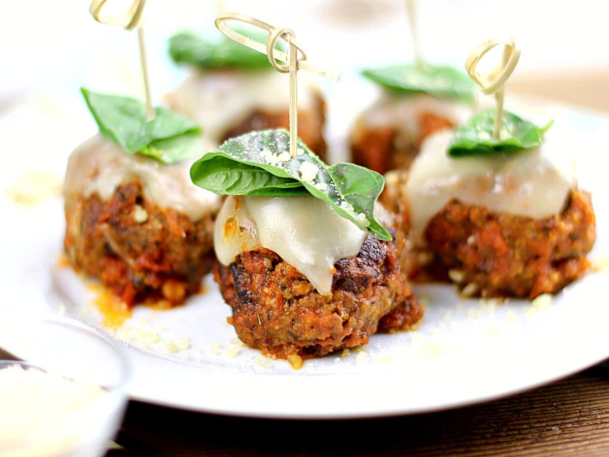 Meatballs appetizer with basil on top on a white plate.