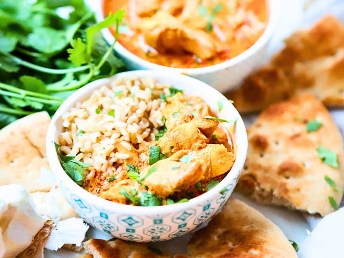 Bowl filled with butter chicken and rice with naan bread next to it.