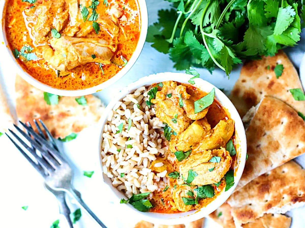 Butter chicken in a bowl with rice topped with parsley.