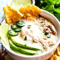 A bowl full of white chicken chili with chips and avocado on top.