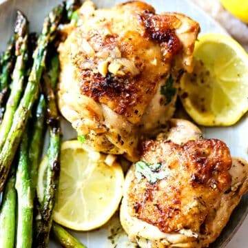 Two pieces of lemon chicken on a plate with asparagus.