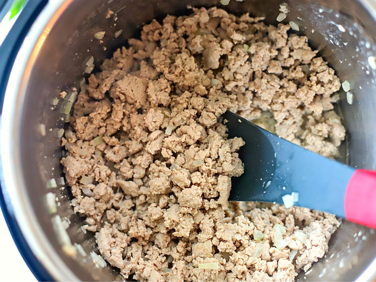 Pressure cooker filled with cooked ground beef, onions, and garlic.