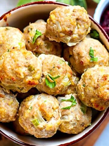 A bowl full of turkey meatballs with herbs on top.