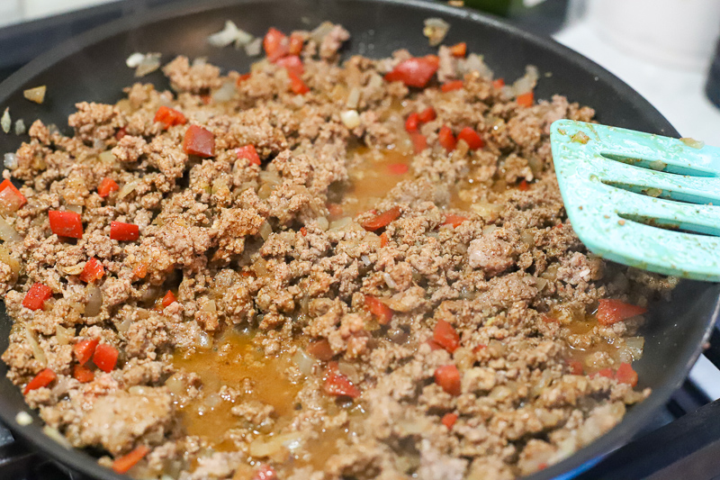 Beef and onions and peppers cooking in a pan.