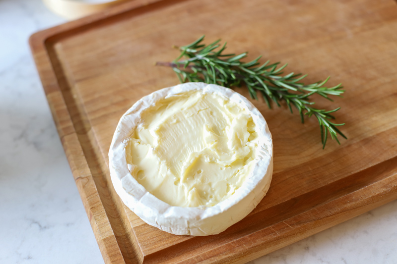 Brie cheese sitting on top of a wooden cutting board.