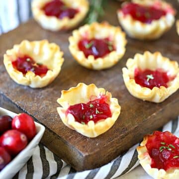 Cranberry brie in phyllo cups on a cutting board.