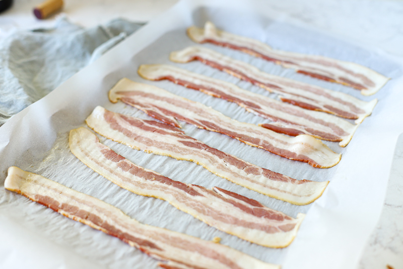 raw bacon on a baking sheet.