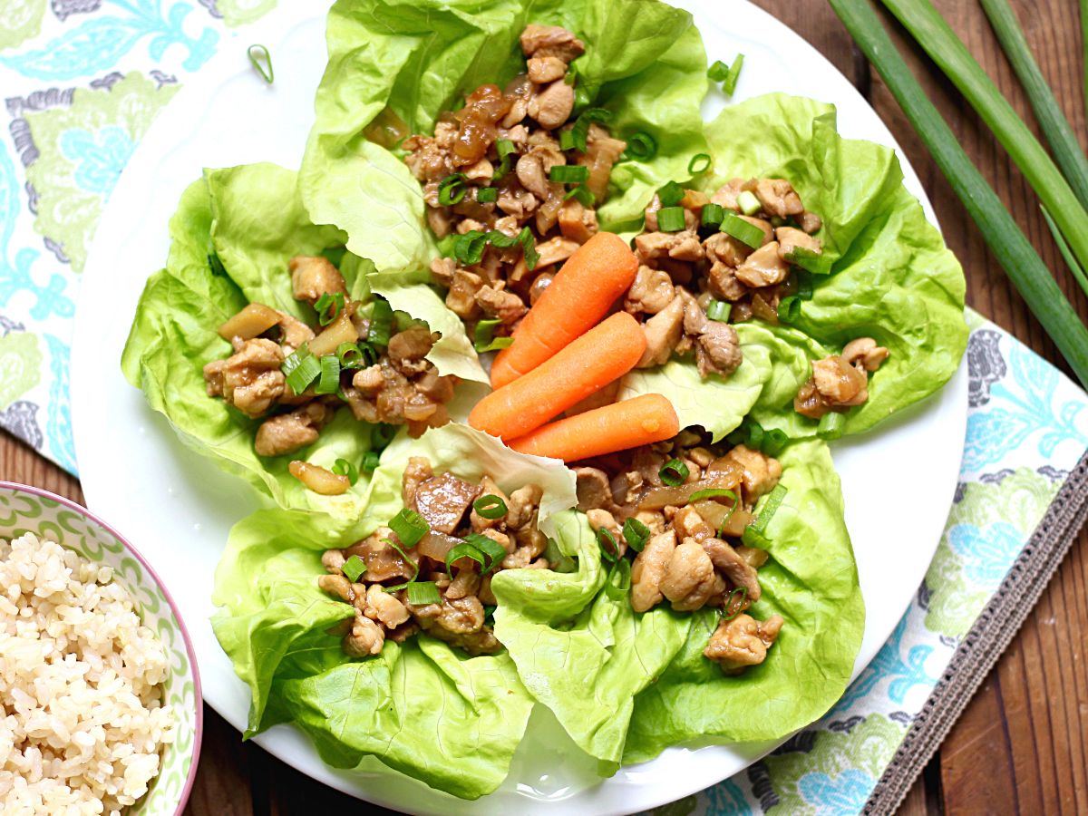 Healthy chicken lettuce wraps on a plate with a  bowl of rice.