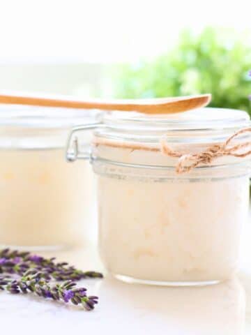 A container of lavender vanilla sugar scrub with a piece of lavender next to it.