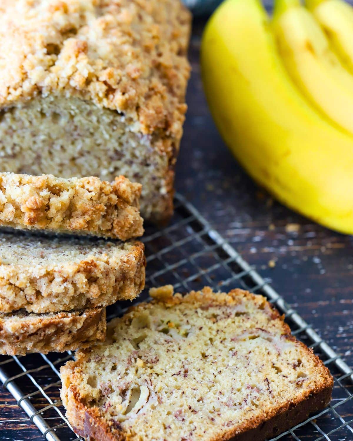 Banana Bread on a cooling rack with a bunch of bananas next to it.