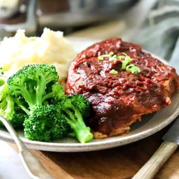 BBQ pork chop cooked in the crockpot on a plate with broccoli.