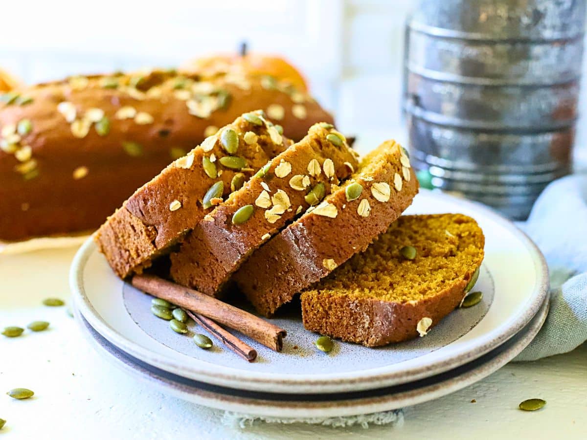 Plate with sliced pumpkin bread with cinnamon sticks next to it.