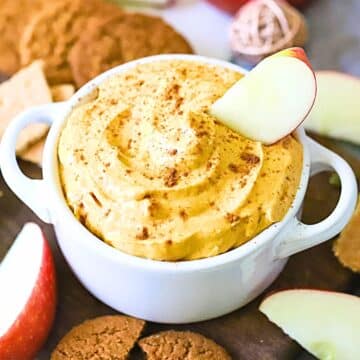 A bowl full of pumpkin dip with apples around it.