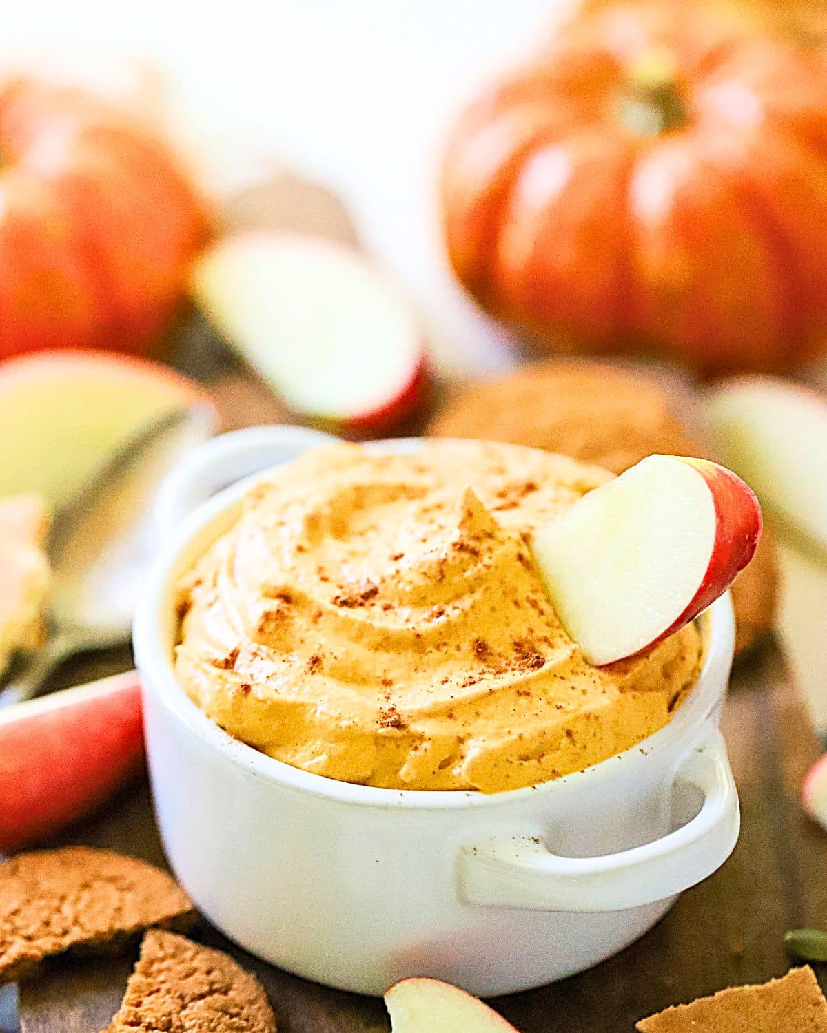 A small bowl full of pumpkin dip with an apple sticking out.