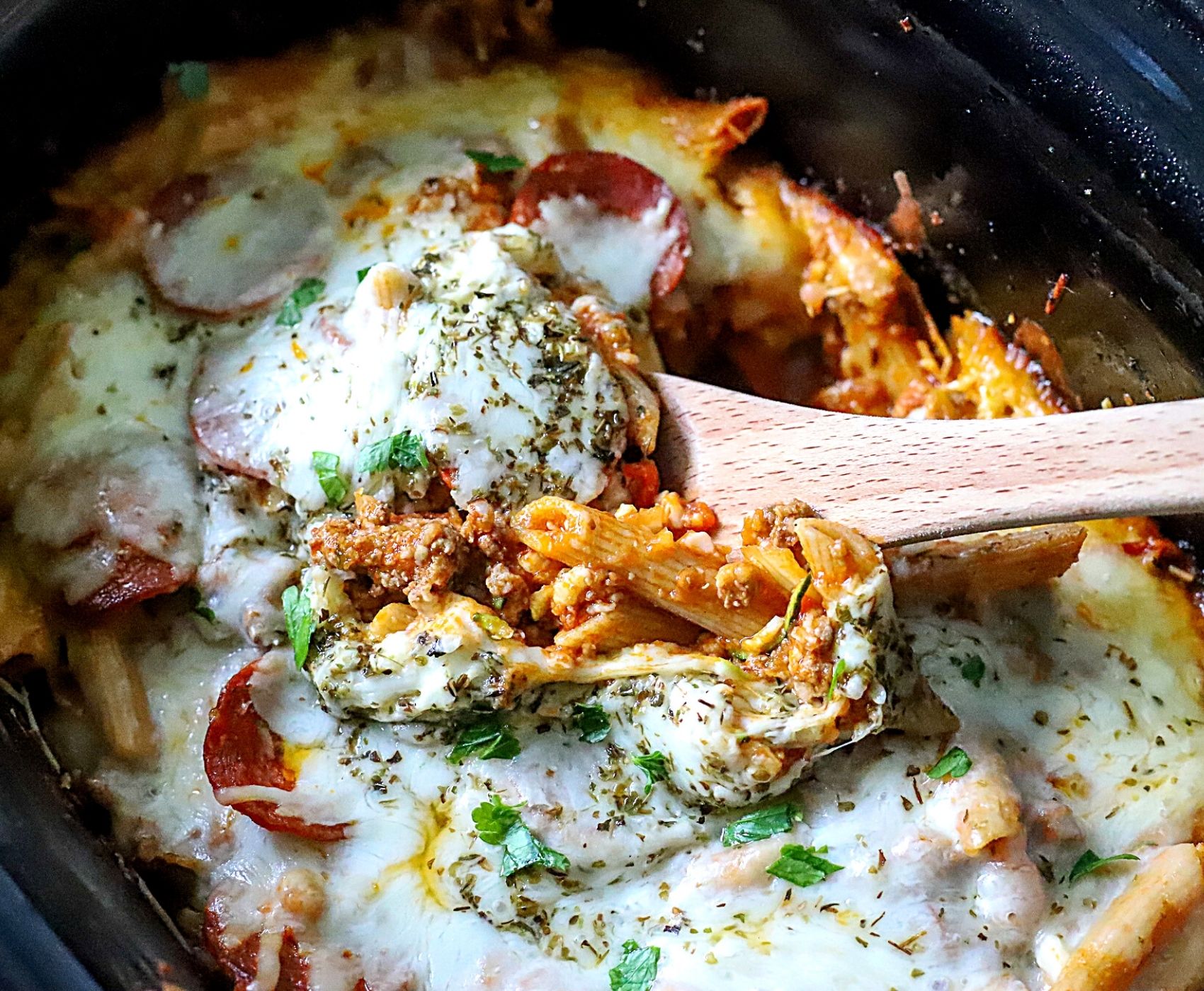 slow cooker pizza casserole with a serving spoon in it. 