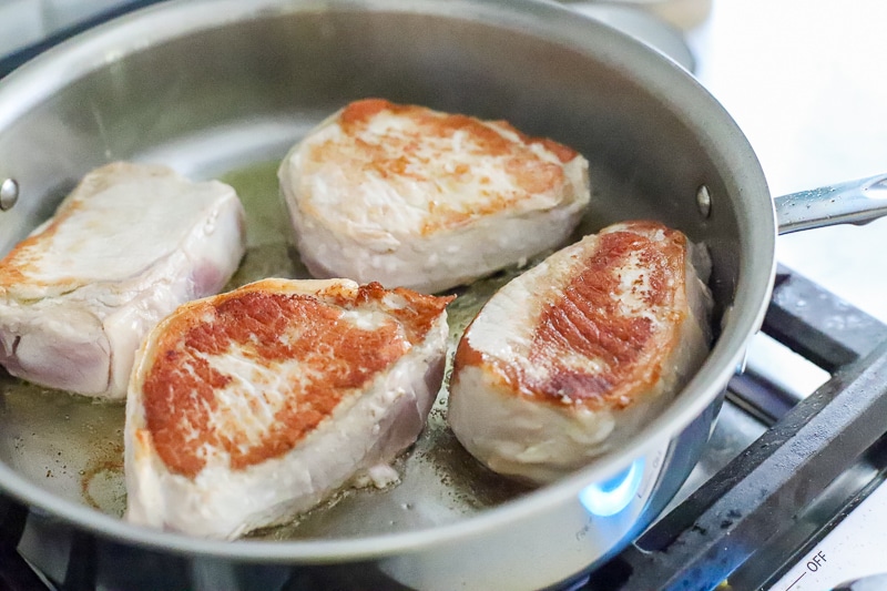 pork chops being fried in a pan