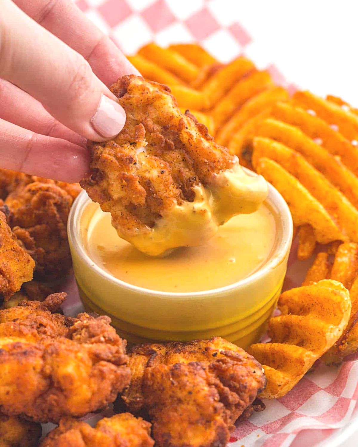 Chicken fingers being dipping in Chick-fil-A sauce.