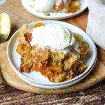 slow cooker peach cobbler on a plate with ice cream.