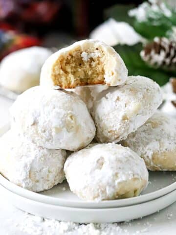 Snowball cookies rolled in powdered sugar stacked on a white plate.