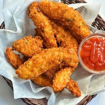 Crispy chicken tenders in a basket with dipping sauce.