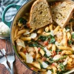 Pot full of chicken spinach pasta with garlic bread slices on top.