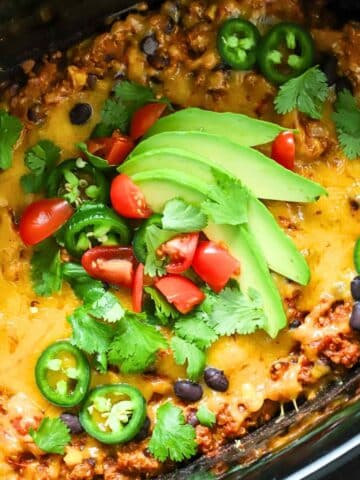 Mexican casserole with ground beef topped with avocado in a crock pot.