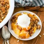 A plate with a homemade peach crisp topped with a scoop of ice cream.