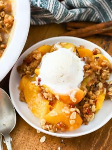 A plate with a homemade peach crisp topped with a scoop of ice cream.