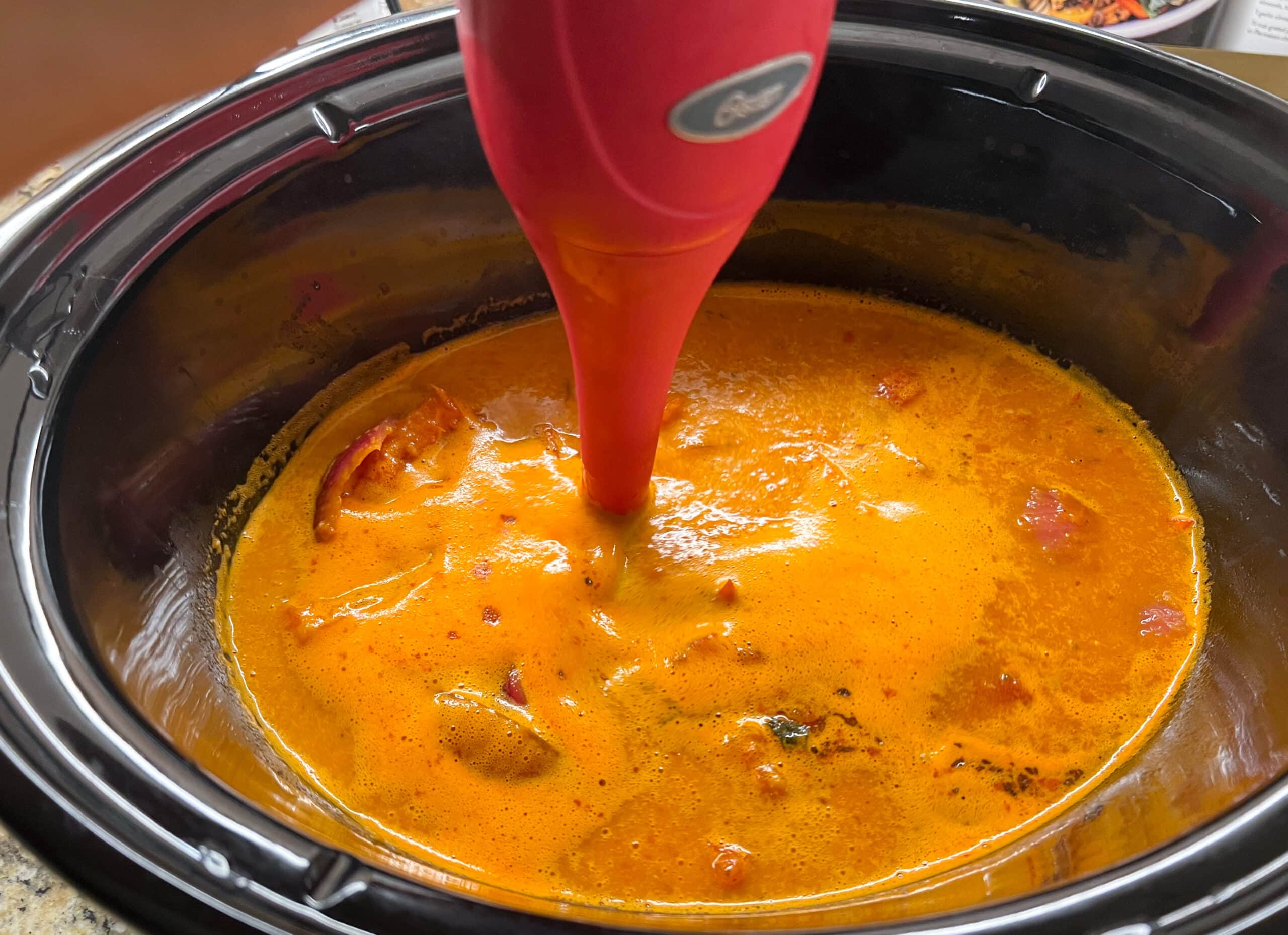 Immersion blender blending Tomato Basil soup ingredients in slow cooker