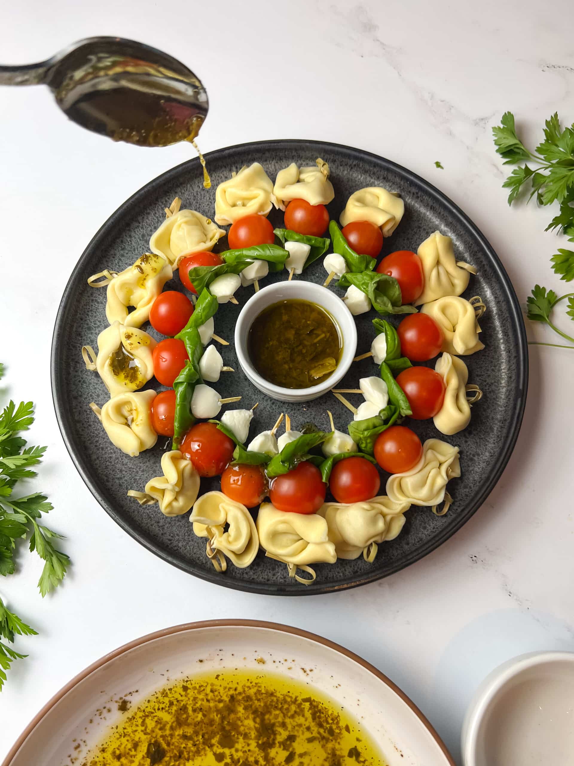 Drizzling dressing over tortellini caprese skewers