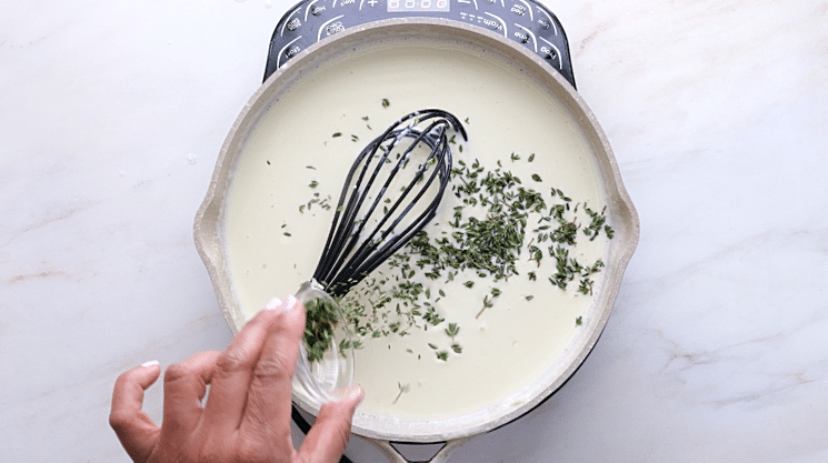 Adding thyme to cheese sauce in saucepan