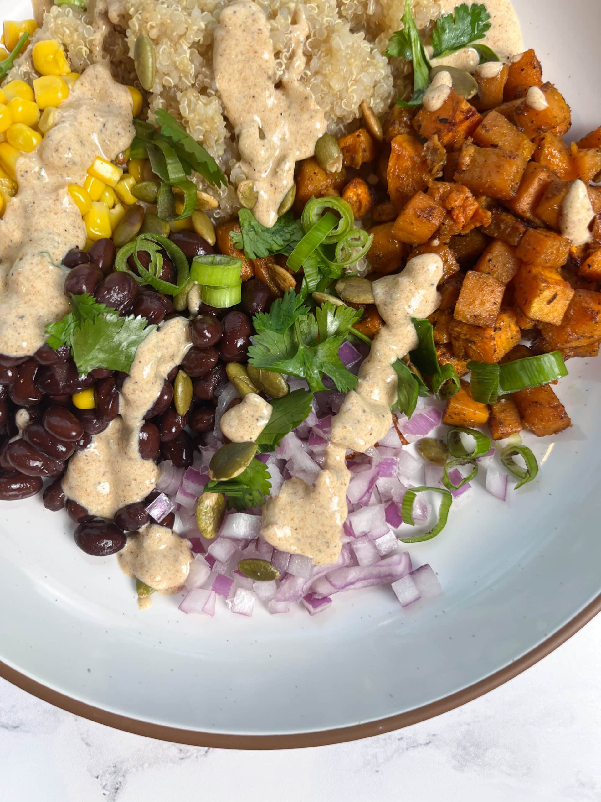 Roasted Sweet Potato and Black Bean Quinoa Bowl with dressing drizzled over