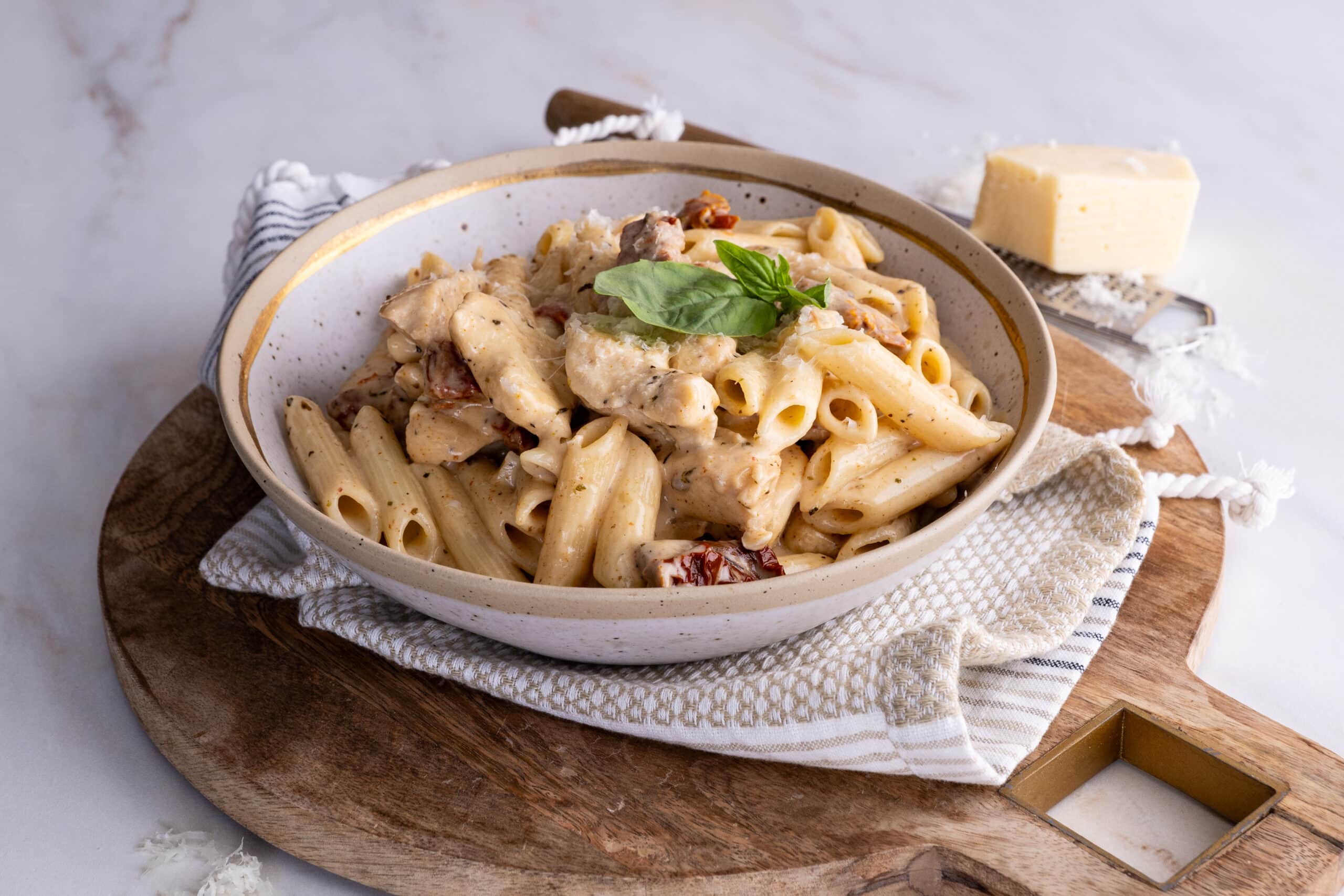 Side photograph of Marry Me Chicken and Penne Pasta in a bowl garnished with freshly grated parmesan and fresh basil leaves