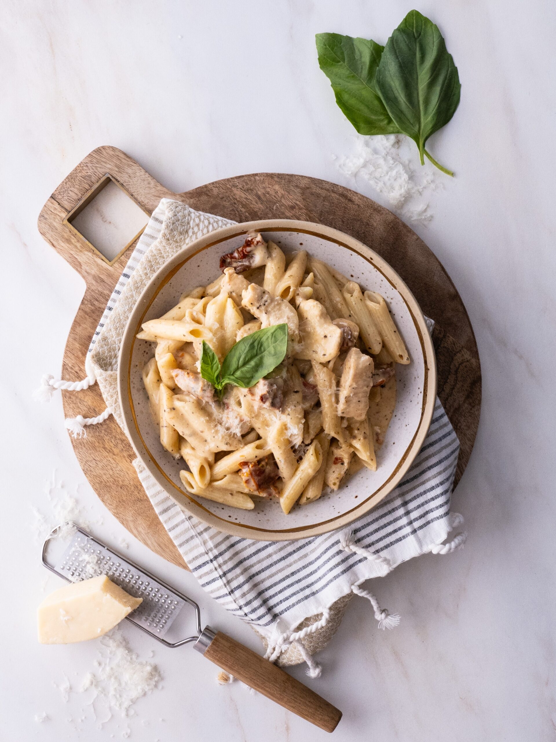 Marry Me Chicken and Penne Pasta in a bowl garnished with freshly grated parmesan and fresh basil leaves