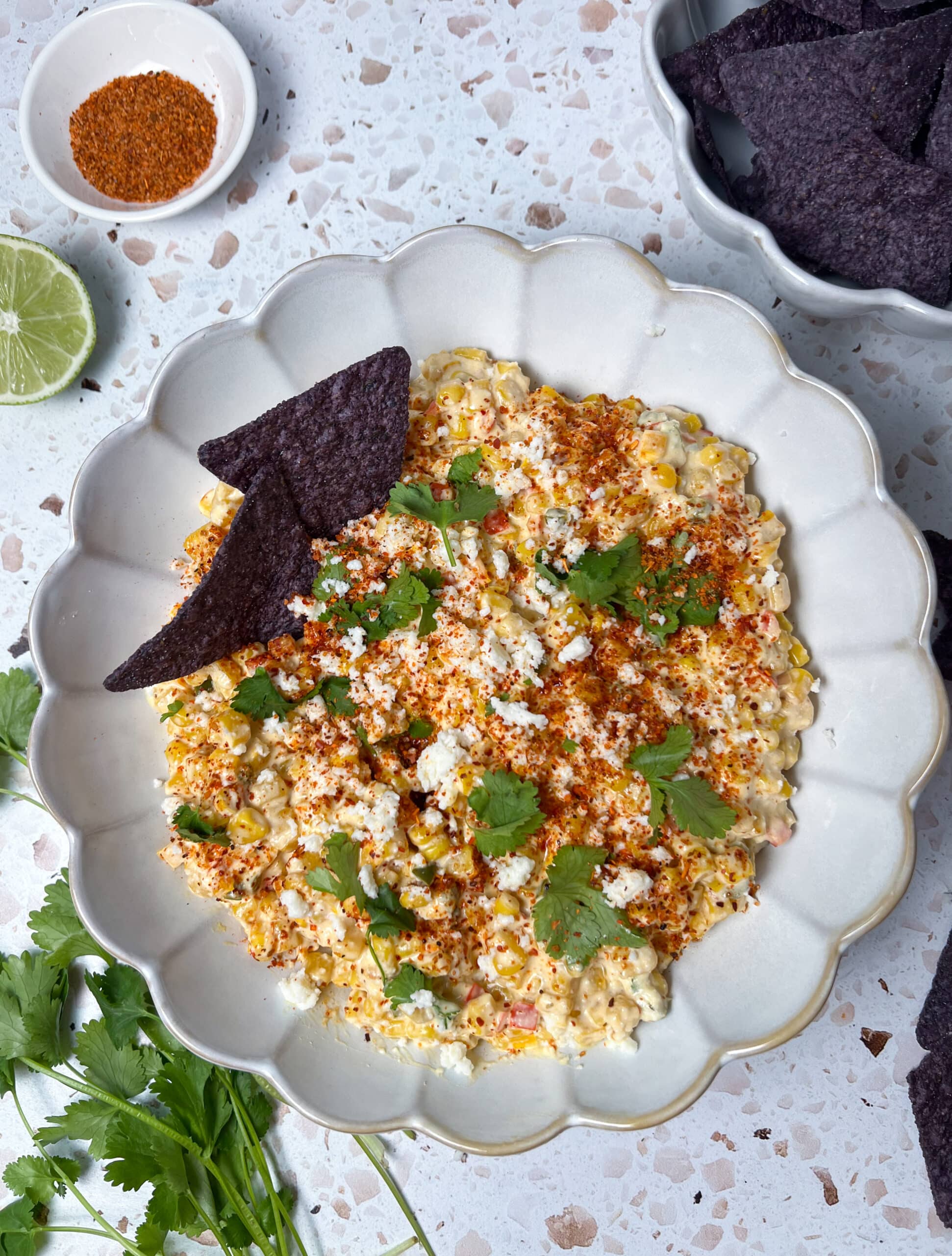 Top down picture of elote corn dip in a scalloped bowl topped with cilantro, extra cojita, and tajin