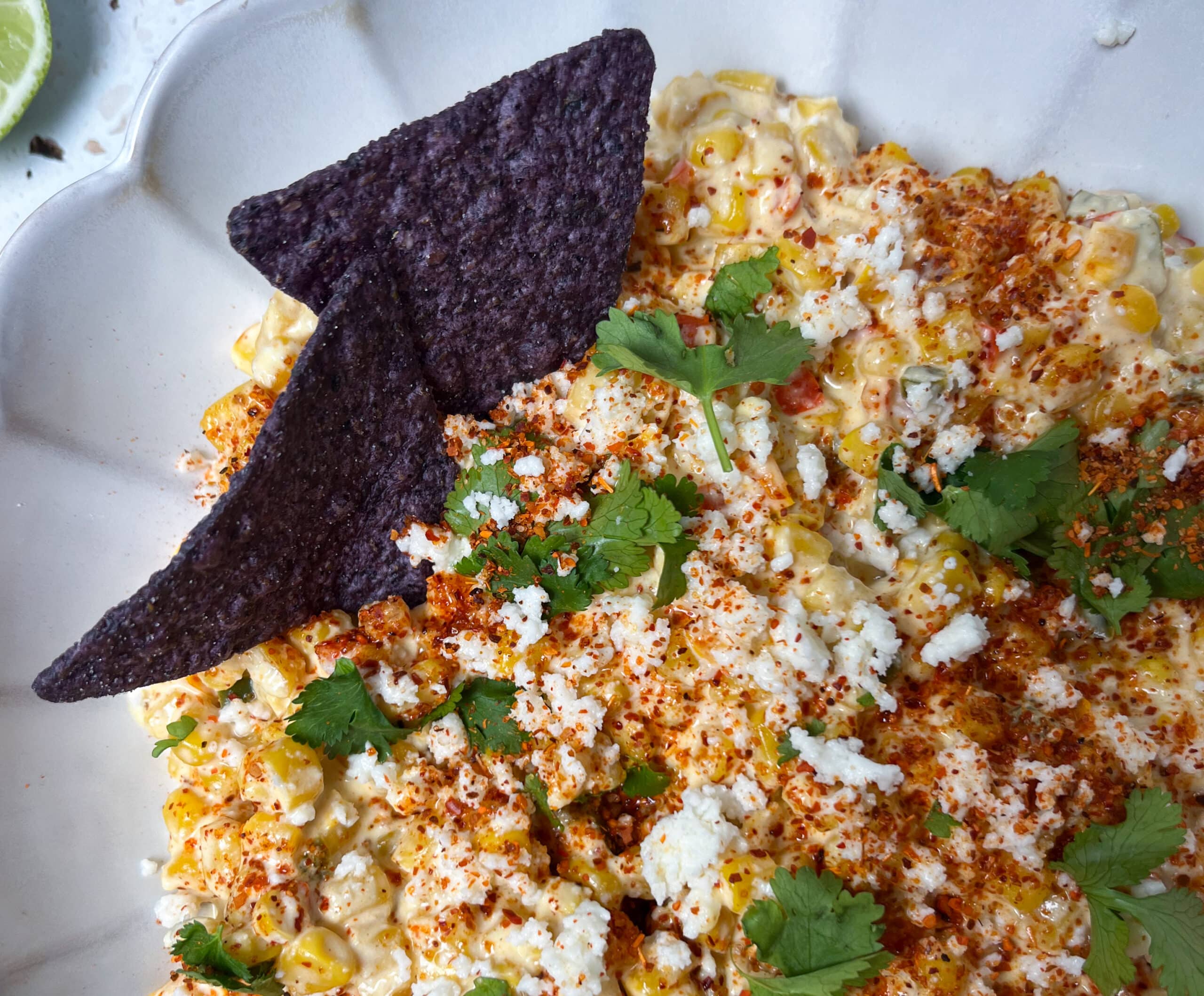 Close-up of elote corn dip topped with cilantro, extra cojita, and tajin with two corn chips