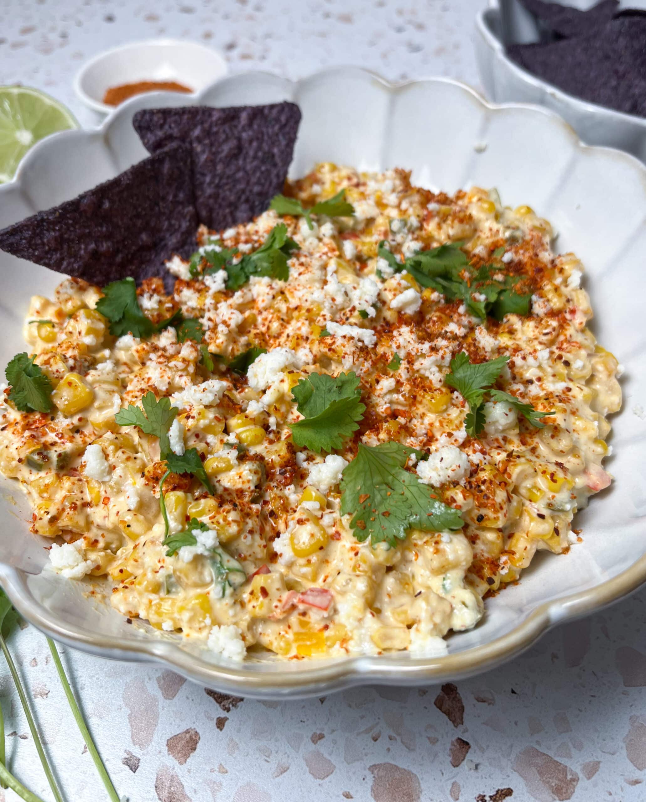 Close-up of elote corn dip topped with cilantro, extra cojita, and tajin