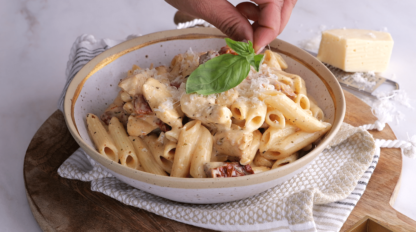 Marry Me Chicken and Penne Pasta in a bowl being garnished with fresh basil leaves