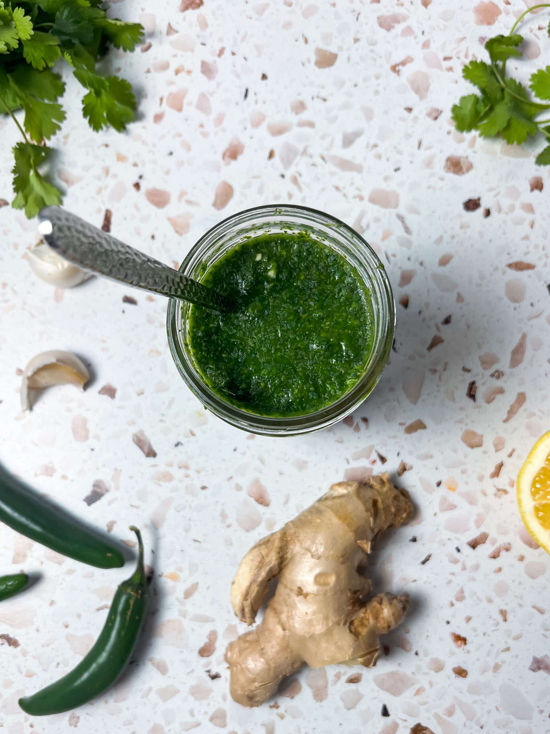 Green chutney in a jar surrounded by ingredients