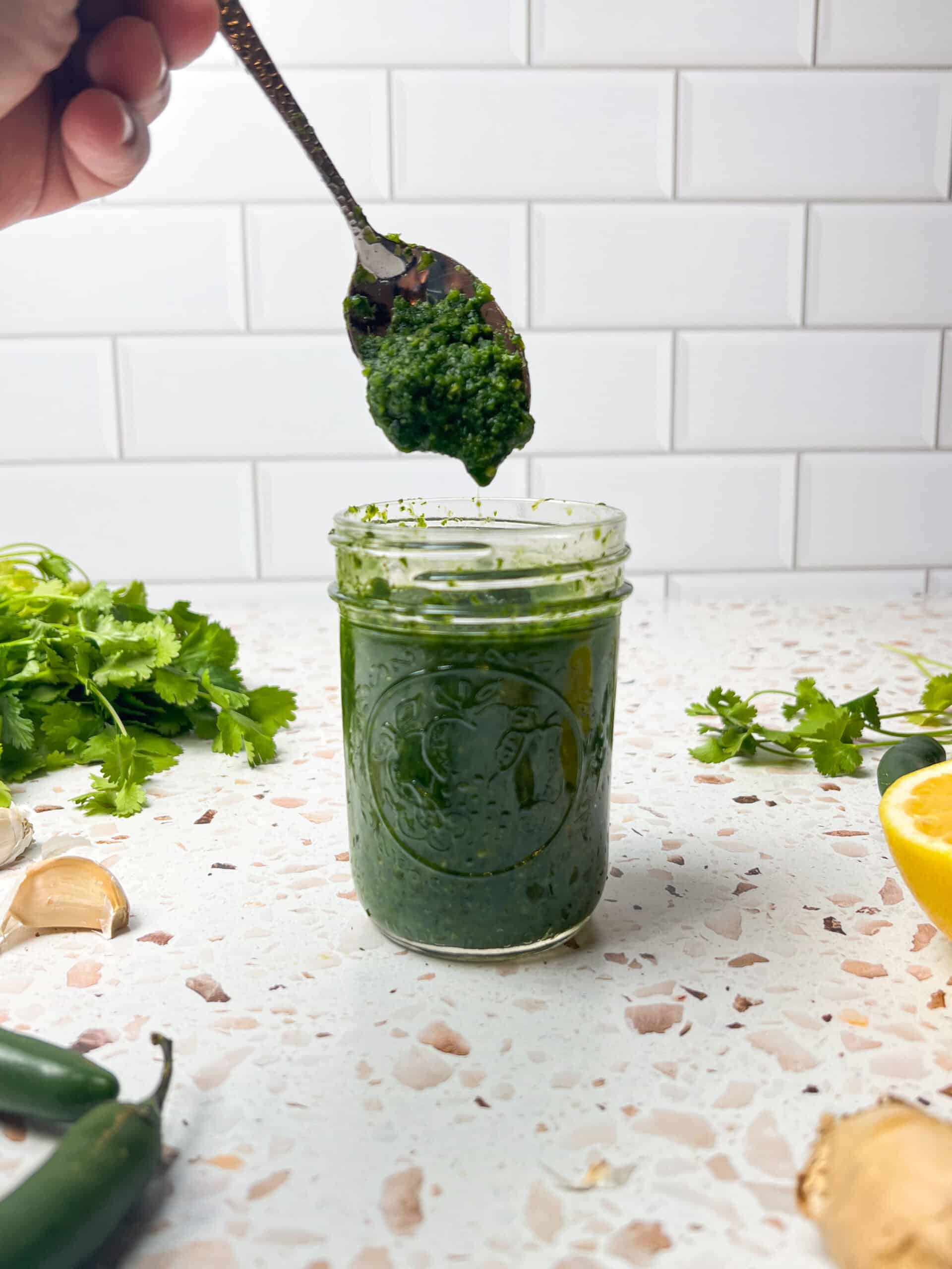 Spoon of Green chutney being taken out from a jar